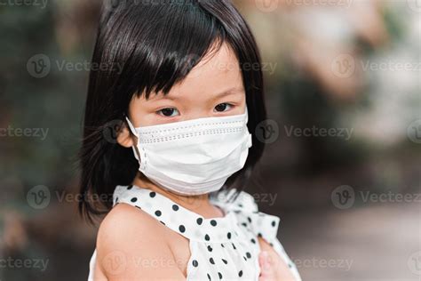 Close up of the face of a cute girl wearing a medical white face mask to prevent the spread of ...