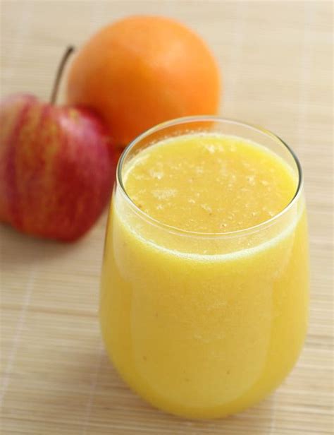 an orange juice in a glass next to two apples