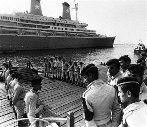 a group of men standing on top of a wooden pier next to a large ship