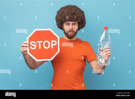 Portrait of serious responsible man with Afro hairstyle wearing orange T-shirt holding red stop ...