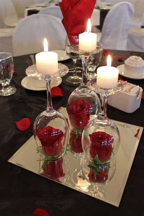 a table topped with wine glasses filled with red roses and floating candle holders covered in water