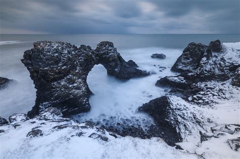 The Arch of Winter - The wonderful natural rock-arch of Gatklettur on a gloomy, snowy winter day ...