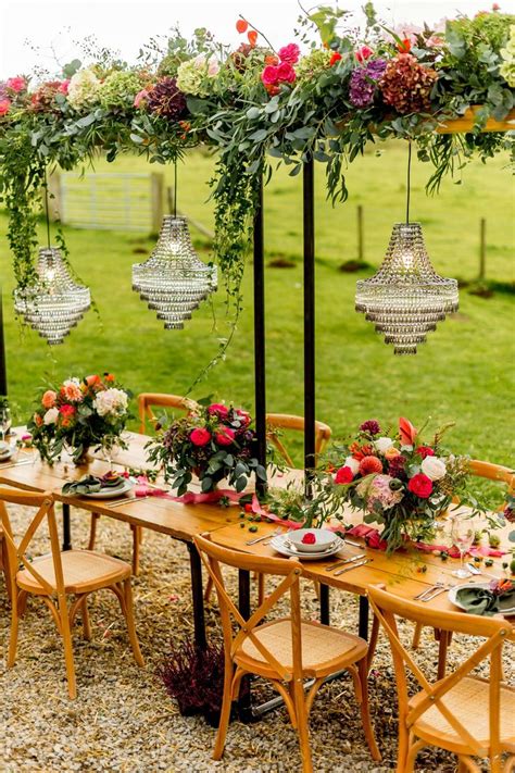 an outdoor dining table set up with hanging chandeliers and floral centerpieces