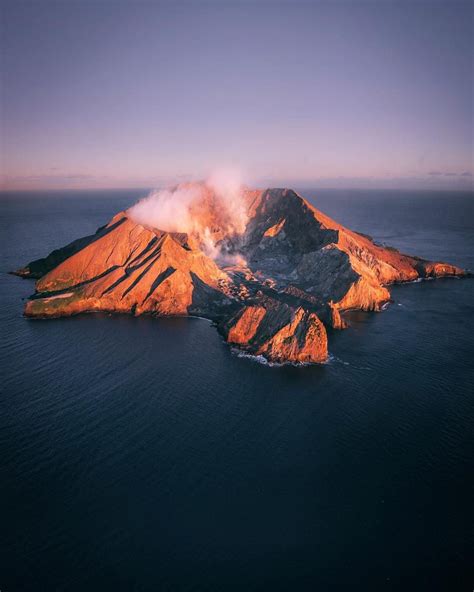 an island in the middle of the ocean with steam rising from it's top