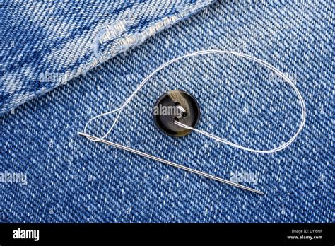 Sewing a button on blue jeans fabric Stock Photo - Alamy