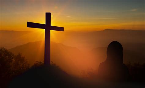 Silhouette of woman holding a bible praying In front of the cross on sunset background ...