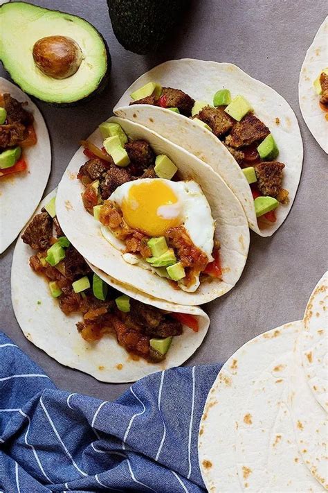 several tacos with meat, avocado and an egg on the top one