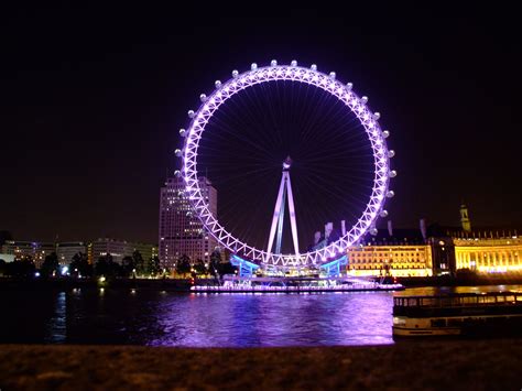 a ferris wheel lit up in the night sky over water with buildings and lights behind it