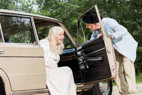 senior man opening car door in front of beautiful woman - Stock Photo - Dissolve