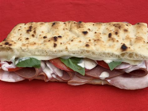 Italian-inspired warm flatbread sandwich with ham, salami, melted mozzarella cheese, tomatoes ...