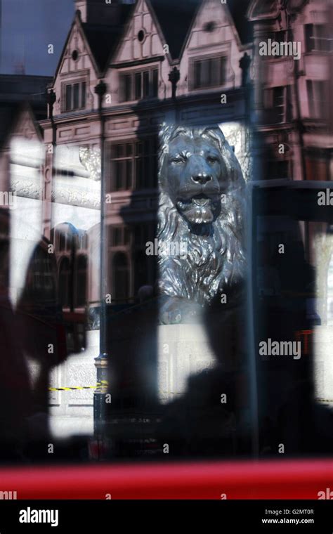 Silhouettes in a red London bus, reflections on its side and a view of a Lion statue in ...