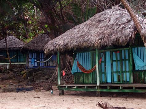 a hut on the beach with hammocks hanging from it's roof and windows