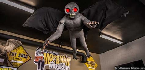 Mothman costume hangs from the museum ceiling, with a gray body, large black wings, hands with ...