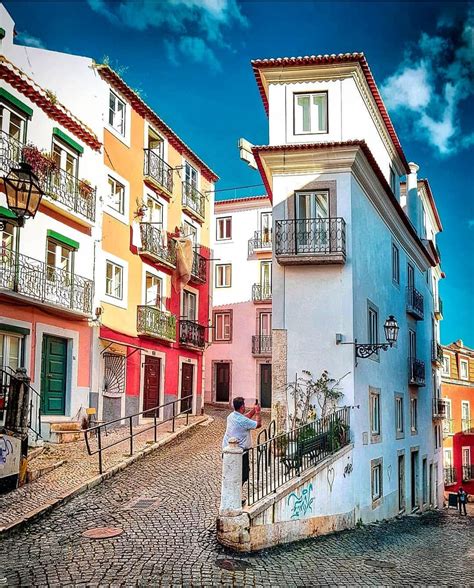 a man standing on the side of a cobblestone road next to tall buildings