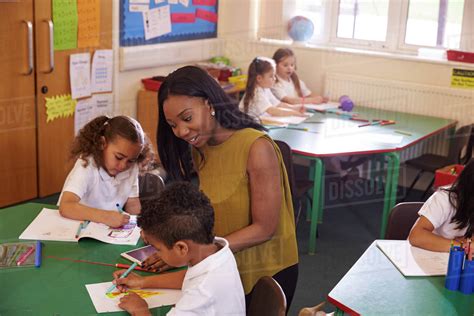 Female elementary school teacher helping pupils at desk - Stock Photo ...