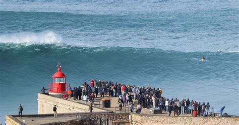 People watching the big giant waves crashing near the Fort of Nazare Lighthouse in Nazare ...