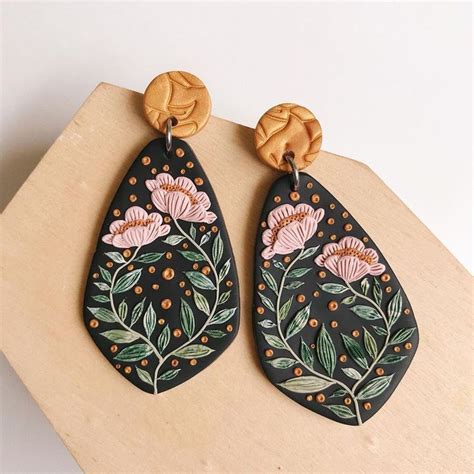 two wooden earrings with flowers painted on them are sitting on a piece of wood that is laying ...