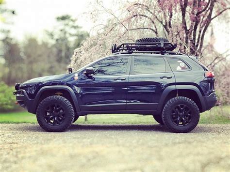 a blue jeep parked on the side of a dirt road next to trees with pink flowers