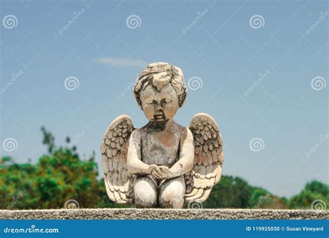 Closeup of Praying Baby Angel Statue on Tombstone with Trees and Blue ...