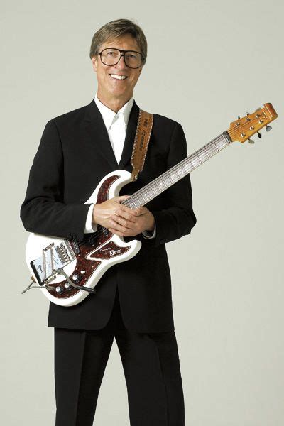 a man in a black suit holding a guitar and posing for the camera with his hands on his hips