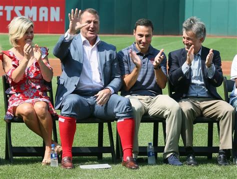 three men and two women are sitting on a bench at a baseball game, clapping