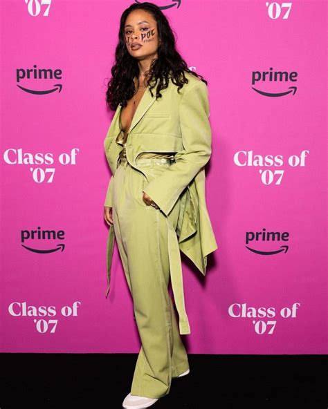 a woman standing in front of a pink wall wearing a green suit and white shoes