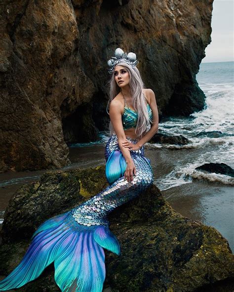 a beautiful mermaid sitting on top of a rock next to the ocean