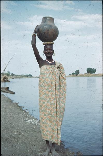 a woman carrying a pot on her head by the water