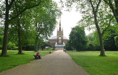 two people sitting on benches in the middle of a park with trees lining both sides