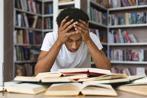 Exhausted black guy holding his head and reading book in library Stock ...