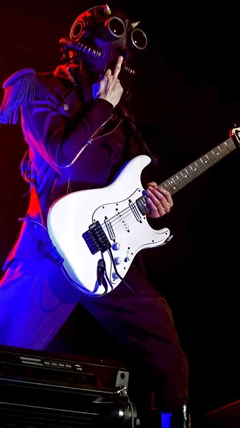 a man with glasses on his face playing an electric guitar in front of a microphone