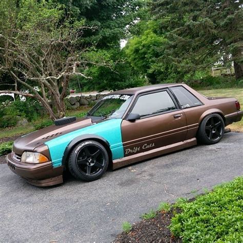 a brown and blue car parked on the side of a road next to some trees