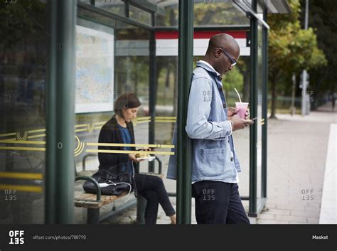 Mid adult commuters waiting at bus stop in city stock photo - OFFSET