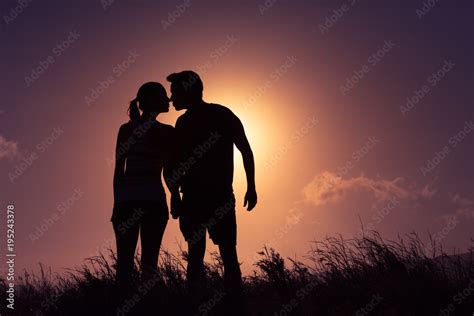 Silhouette of young couple holding holding hands kissing at sunset. Love and relationships ...