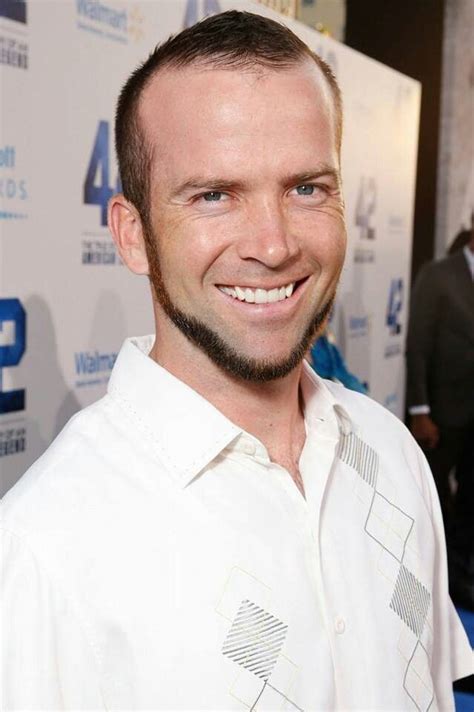 a man with a goatee smiles at the camera while standing in front of a blue carpet