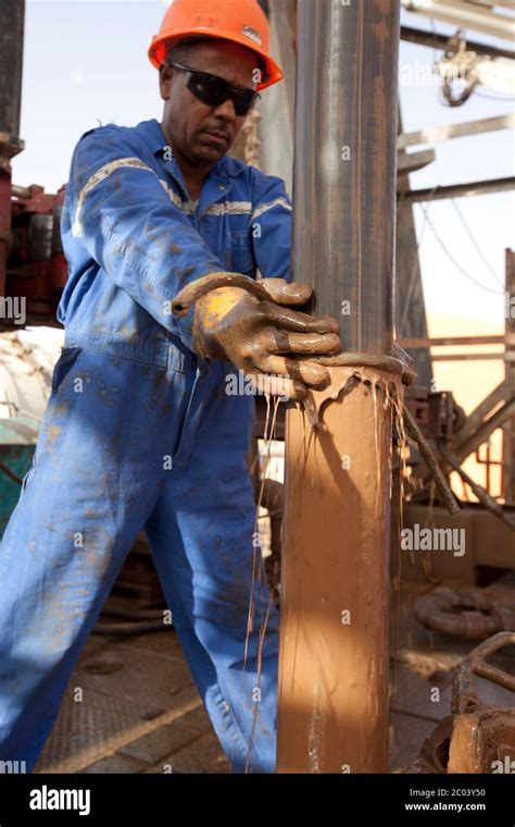 A drill rig roughneck wipes drill mud from pipe being lifted from an ...