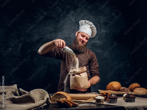 A bearded baker wearing a cook uniform sprinkling some flour in bag ...