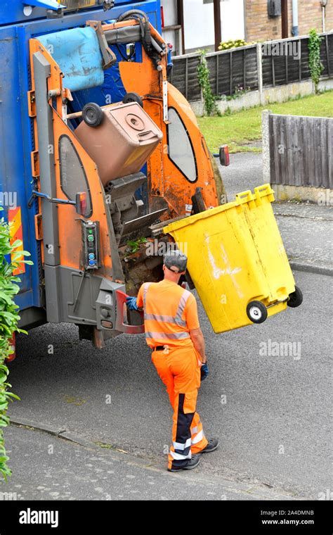 Refuse collection wearing high vis clothes operates lifting up controls back of dustcart to ...