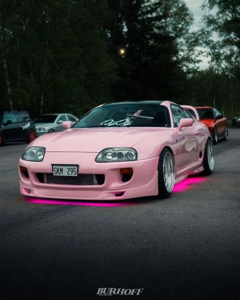 a pink sports car parked in a parking lot next to other cars with neon lights on them