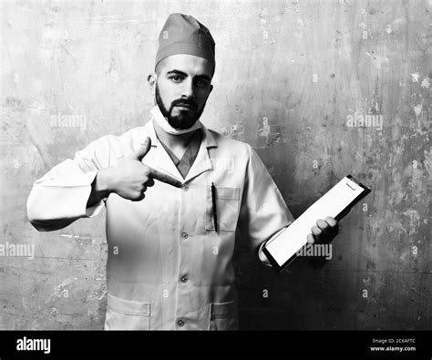 Doctor in uniform with beard and serious face expression pointing at clip folder on background ...