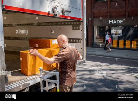 A UPS van driver unloads a stack of boxes from the rear of his vehicle ...