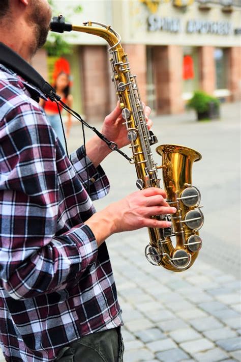 Man Sitting on Stool While Playing Saxophone Beside Fence · Free Stock Photo