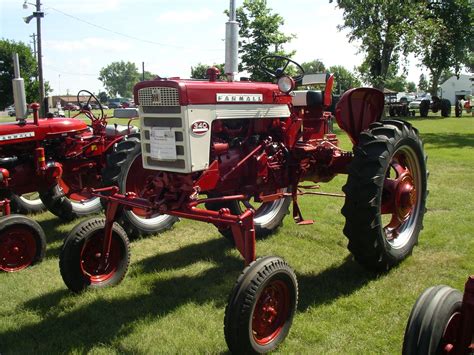 an old red farmall tractor parked on the grass in front of other antique tractors