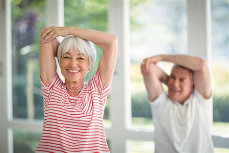 Happy senior couple performing stretching exercise at home - Omni-Fitt