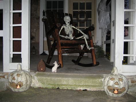 Spooky Halloween skeleton in rocking chair on porch with lighted pumpkins and a rat.