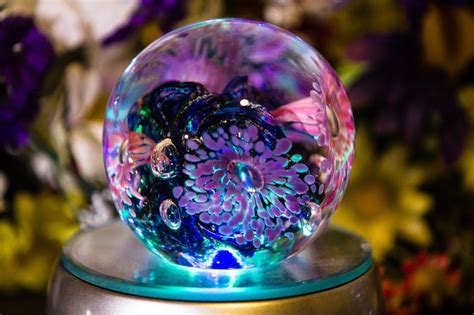 a colorful glass ball sitting on top of a metal stand with flowers in ...