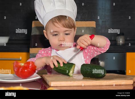 Funny kid sitting on the kitchen table. child cucumber with a knife cuts Stock Photo - Alamy