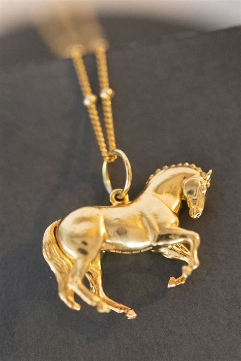 a gold necklace with a horse on it's back end, sitting on a black surface