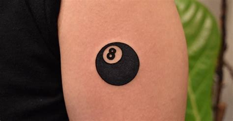 Minimalist eight-ball tattoo on the upper arm.