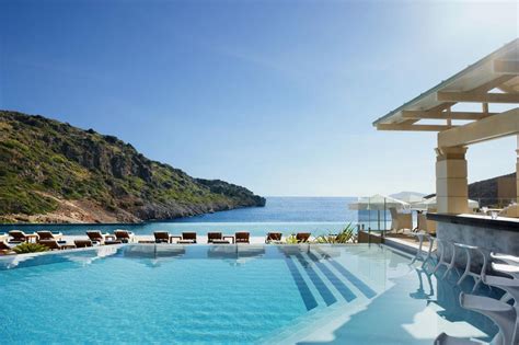 an outdoor swimming pool with chairs and umbrellas next to the ocean on a sunny day